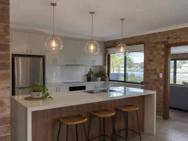 Kitchen with three glass pendant lights over an island, white cabinets and brick walls in Paradise Point