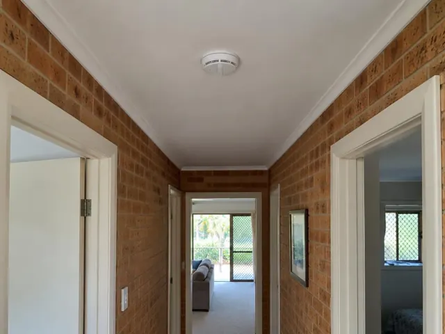 Hallway ceiling smoke alarm in a brick home interior in Biggera Waters
